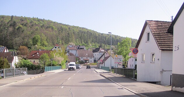 Das Foto zeigt die Brücke über den Neumühlkanal in Blaubeuren-Gerhausen. Mehrere Wohnhäuser und im Hintergrund ein Wald.
